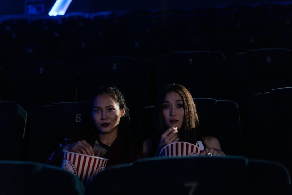 Two women with popcorn watching a film in a dark cinema