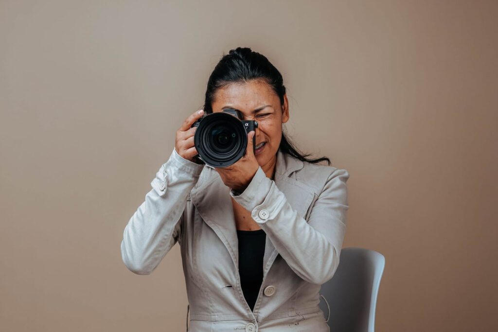 Female photographer aiming a camera with a large portrait lens toward the viewer