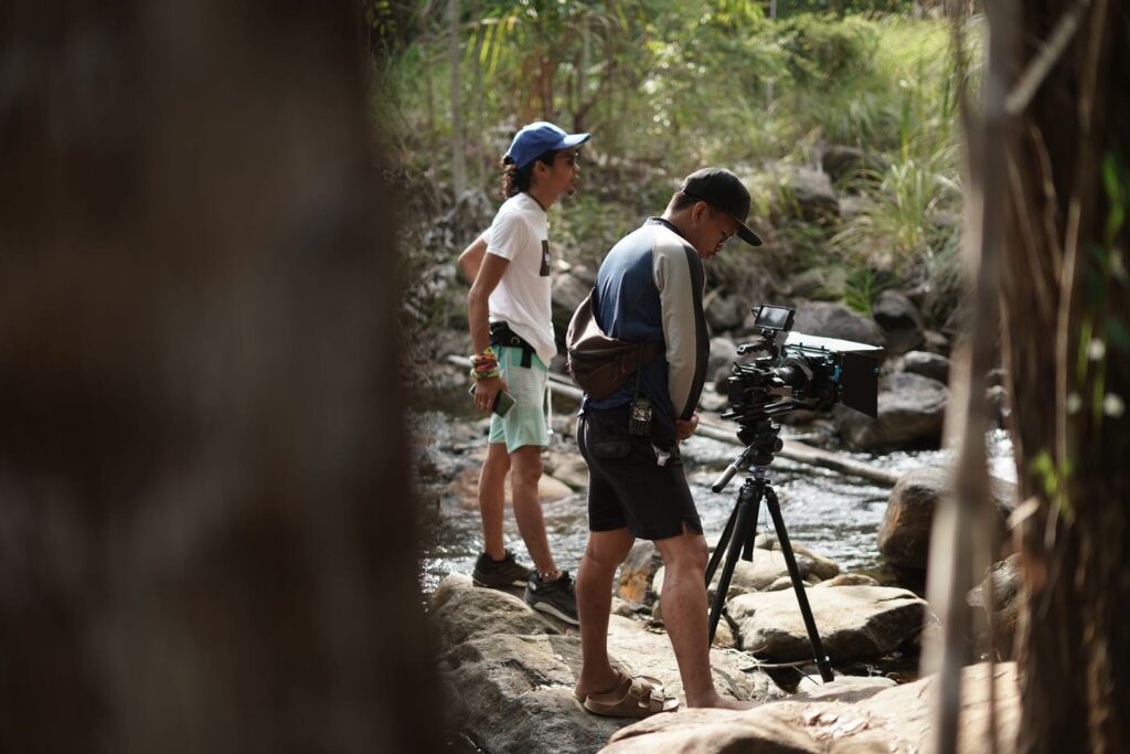 Two filmmakers setting up a camera on a tripod beside a rocky stream