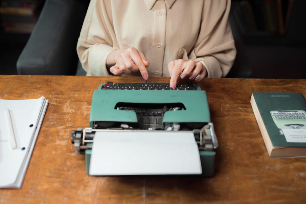 Hands typing on a vintage green typewriter on a wooden desk