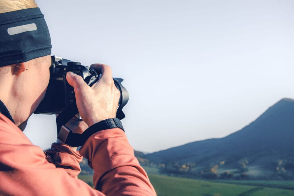 Photographer framing a shot of green hills and a mountain peak